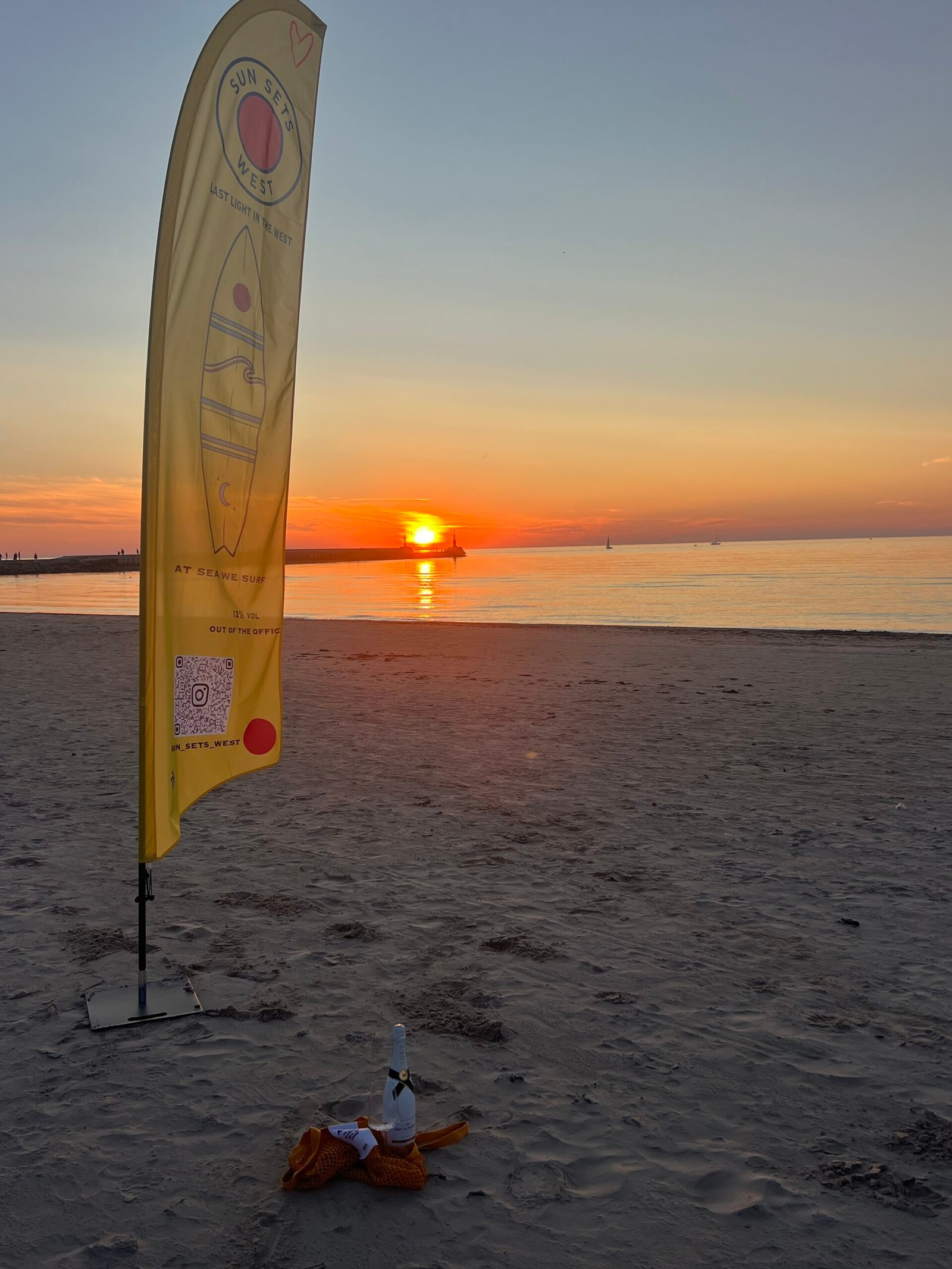 The sun setting over the sea beside a Sun Sets West flag